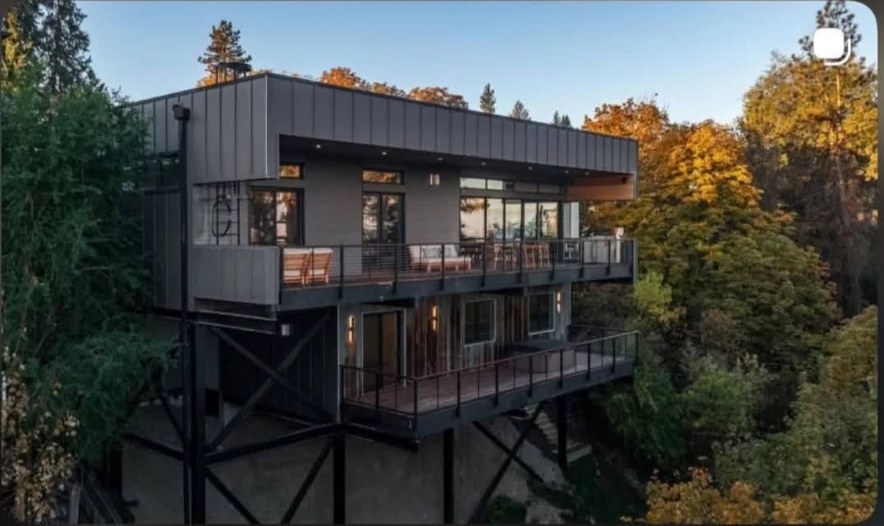 Modern hillside home with dark standing seam metal roofing and siding at sunset