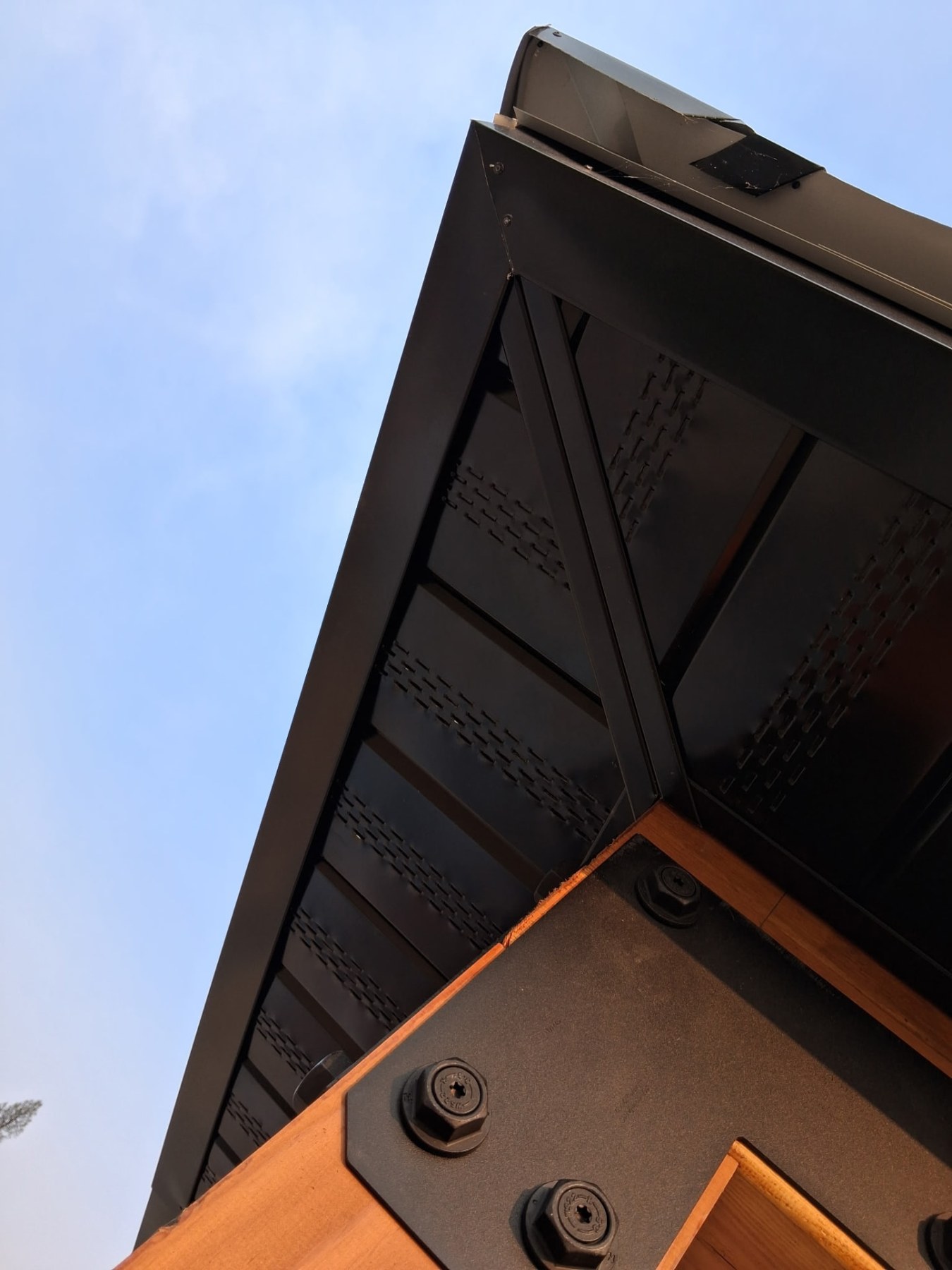 Close-up of black metal roof edge, vented soffit and a cedar beam with heavy black bolts